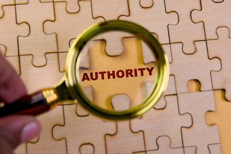 A hand holds a magnifying glass over a puzzle piece with the word authority, illustrating clarity and focus.の写真素材