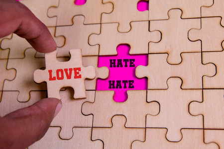 A hand places a love piece into a puzzle showcasing contrasts between love and hate.の写真素材