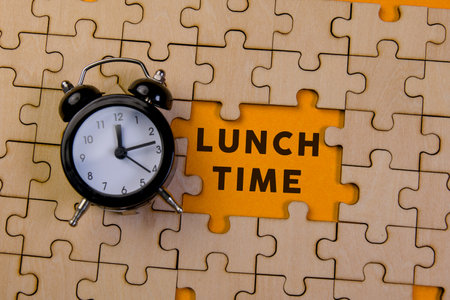 A black alarm clock rests on a yellow puzzle piece marked with lunch time, symbolizing break and relaxation.の写真素材