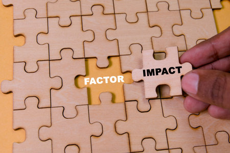 A hand places a puzzle piece labeled Factor into a board, highlighting the link to Impact in a thoughtful arrangement.の写真素材