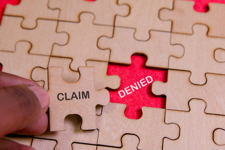 A hand holds a puzzle piece labeled claim, placed near a denied piece, symbolizing insurance processes.の写真素材