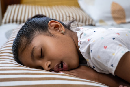 A young girl enjoys a deep sleep, resting her head on a soft striped pillow in a warm, inviting bedroom.の写真素材