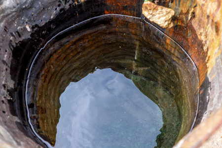 Water fills a deep well with stone walls, reflecting light and surroundings, showing textures of the stones.の写真素材