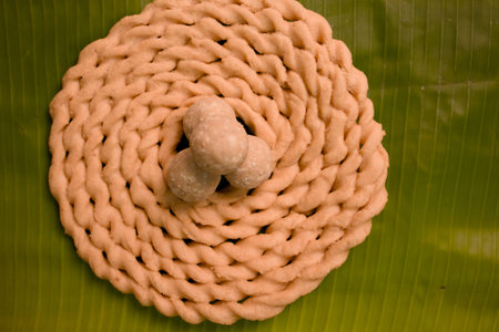 Cook is making a spiral shaped snack with dough placed on a banana leaf.