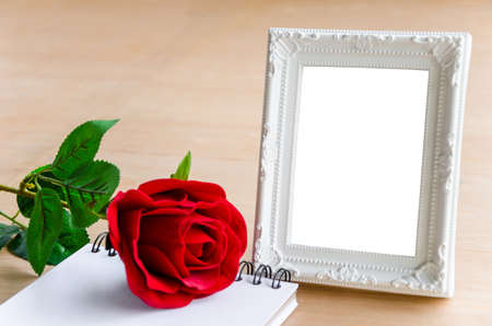 White vintage photo frame and red rose with blank diary on wooden background. の写真素材