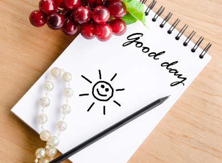 Good day wording on white diary and red grape on wooden background.