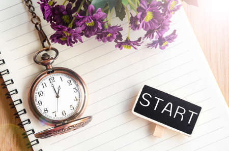 Start in black wooden tag and pocket watch at 1 pm with open diary and flower on wooden background....