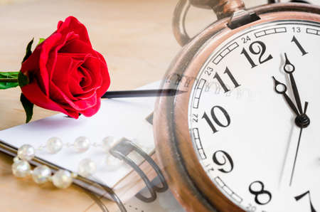 Red Rose and a pocket watch with diary on wooden background.の写真素材