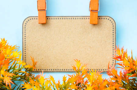 Blank brown tag and wooden clip with yellow leaf on blue blackground.