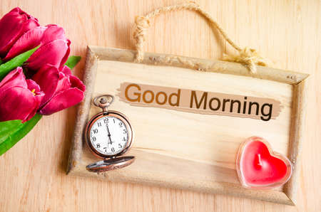 Good morning. Clock and red tulip with red candle heart shape on wooden background.の写真素材