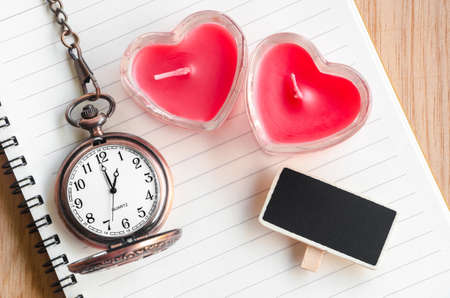 Red heart candle and pocket watch with open diary on wooden background.の写真素材