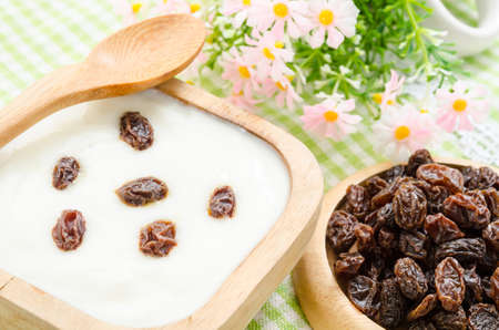 Home sweet yogurt with raisins in a wooden bowl with fower on fabric background.の写真素材