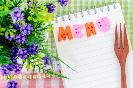 Open diary and wooden spoon fork with flower on beautiful fabric background. Menu concept.の写真素材