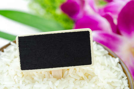 Raw rice and blank black wooden tag for your text with violet orchid on white background.の写真素材