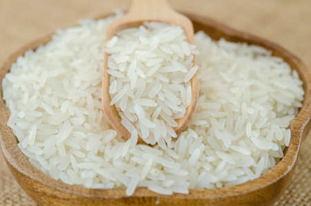Raw rice and wooden spoon in wooden bowl on sack background.の写真素材