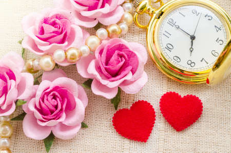 Red heart and pink rose with gold pocket watch on fabric background. Love of time concept.の写真素材