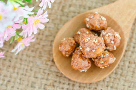 Honey roasted coated peanuts and white sesame seeds in wooden spoon with flower on sack background.の写真素材