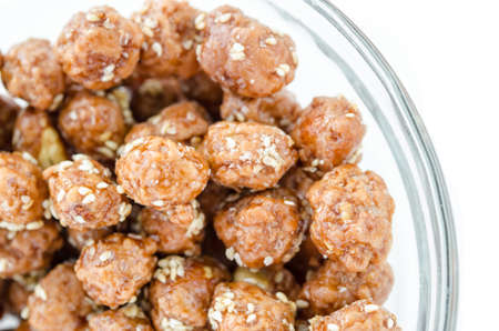 Honey roasted coated peanuts and white sesame seeds in glass bowl on white background.の写真素材