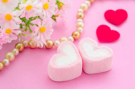 Pink marshmallow herat shape with red paper heart and flower on pink background. Love concept.の写真素材