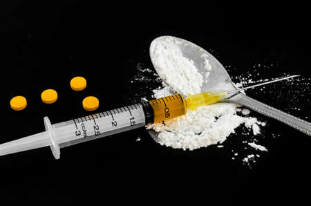 Drug syringe, amphetamine tablets and cooked heroin on spoon.