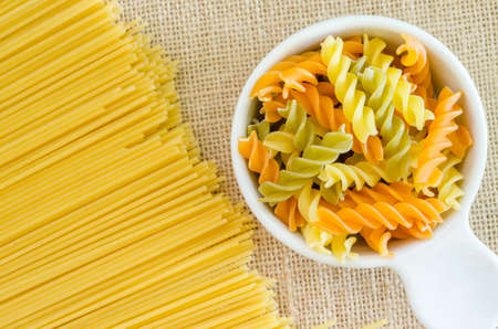 Italian raw pasta with uncooked pasta spaghetti macaroni on sack background.