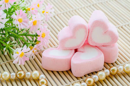 Sweet heart shape of pink marshmallows with flower on mat wooden background,decoration for love and...