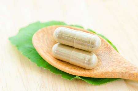 Yellow herbal capsule medical in wooden spoon with green leaf on wooden background.の写真素材
