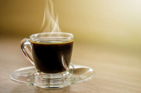 Hot black coffee in glass cup with smoke on wooden table.の写真素材