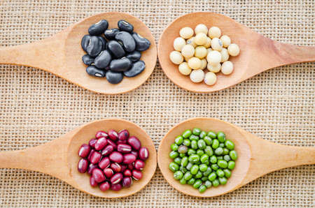 Mix from different beans, black bean, soy bean, azuki bean, mung bean in wooden spoon on the sackcloth backgroundの写真素材