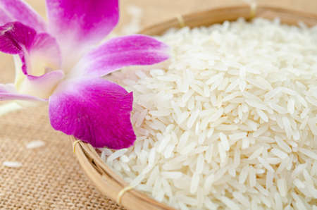 natural organic white rice in basket with orchid on sack background.の写真素材
