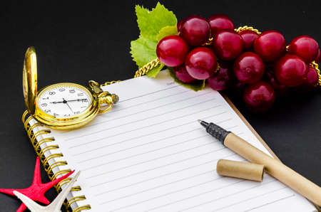 Open diary and golden pocket watch with red grape on black background.の写真素材