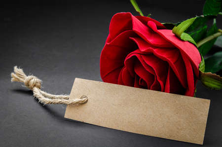 Black recycle brown paper tag with red rose on blackground.の写真素材