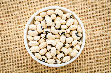 White bowl full of black eyed peas on sack background.の写真素材