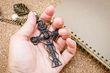 Hand hold vintage crucifix necklace with diary on wooden background.