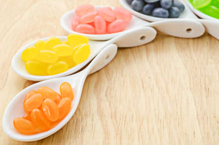 Colorful candies in white spoon on wooden backgroundの写真素材