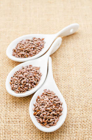 Brown flax seeds or linseed in white spoons on sack background.の写真素材