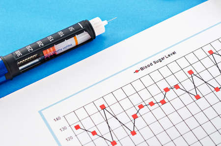 Insulin injection pen with blood sugar level monitoring chart on blue background.の写真素材