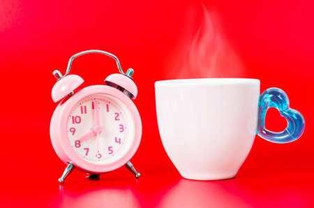 Vintage pink alarm clock with hot coffe and smoke on red background.の写真素材