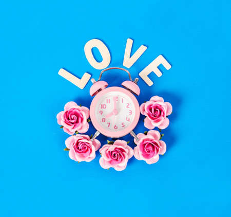 Pink alarm clock and pink rose with love word on blue color background. Valentine concept.の写真素材