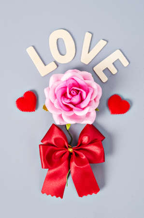 Pink rose and love word with red bow on gray background.の写真素材