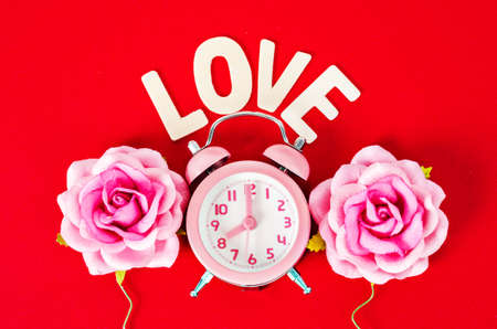 Pink alarm clock  with love wooden word with pink rose on red background. Valentine concept.の写真素材