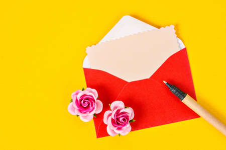 Blank pink paper card in red envelope letter and pen with pink roses on yellow background.の写真素材