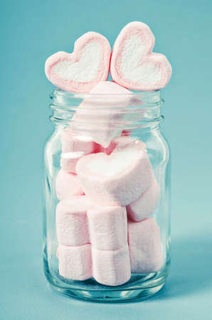 Heart shape pink marshmallows glass bottle on blue background.の写真素材