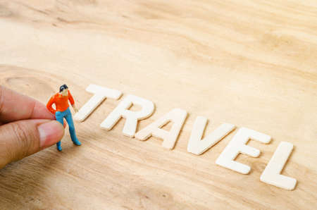 Hand hold miniature figurine of young traveler walking to Travel letters on wooden background.の写真素材