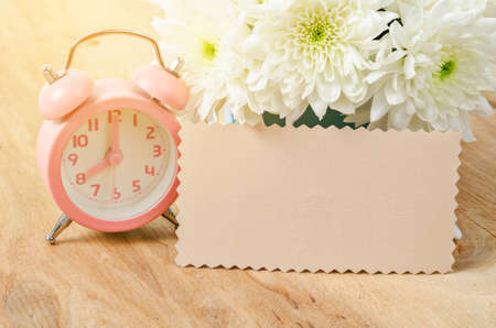 Blank card ready for your text or message and vintage pink alarm clock with white flower on wooden background.の写真素材