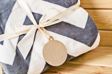 Blanket gift with paper tag on wooden background.