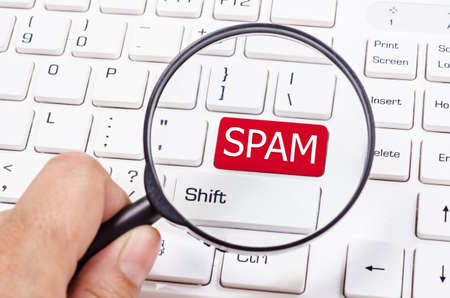 Hand with magnifier. Keyboard of computer or laptop with sign spam