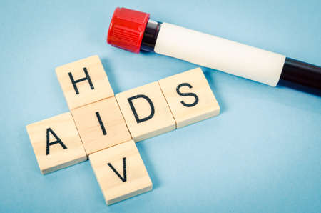Wood blocks spelling out aids with sample blood in tube for test on blue background.の写真素材