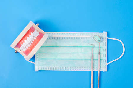 Set of false teeth with dental tools, a stainless steel mirror and face mask on blue background.の写真素材