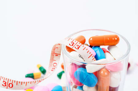 Tape measure and medicine colored in glass on white background.の写真素材